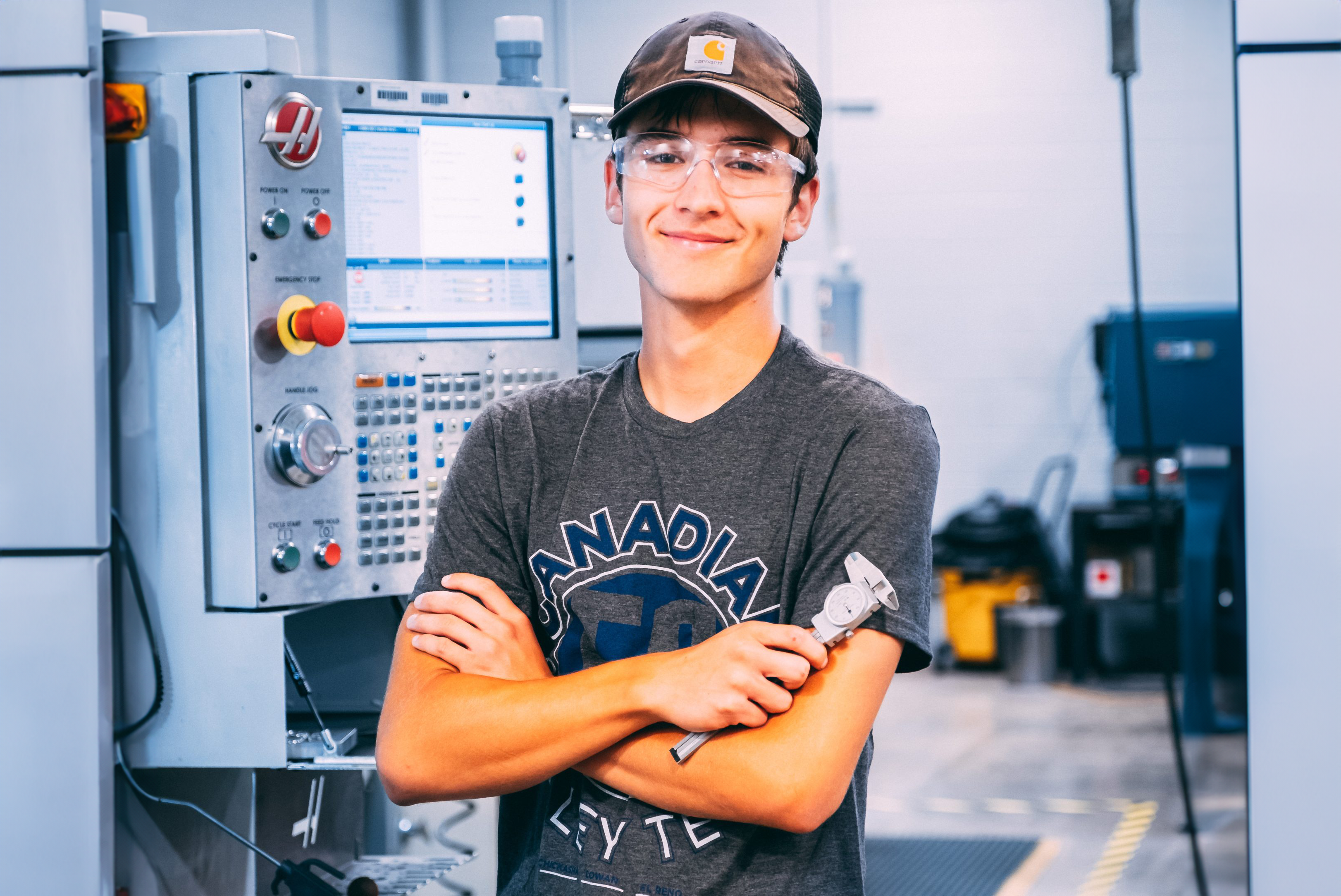 Precision Machining student smiles next to CNC machine while holding a caliper