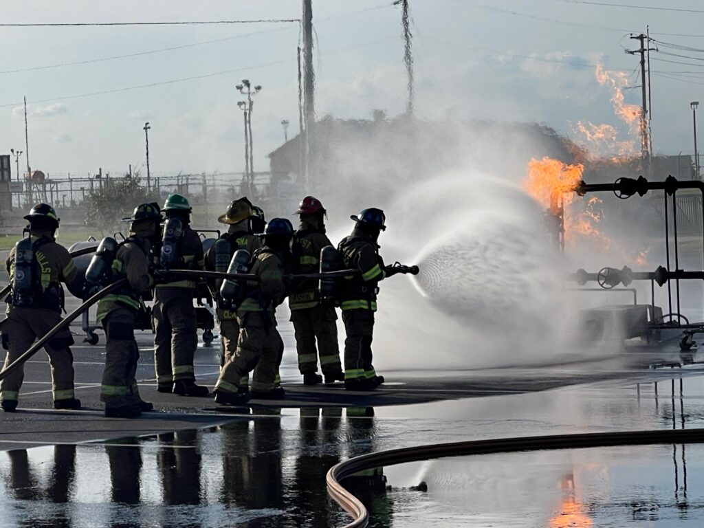 firefighters with hose putting out training fire.